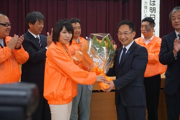 女性が小西先生に花束を渡し周りの人達が拍手をしている写真