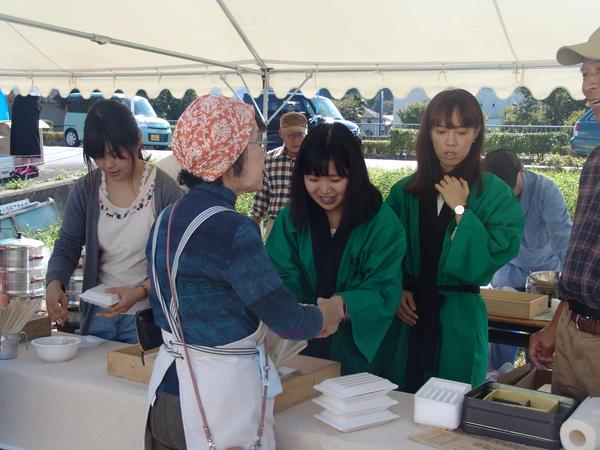 テントの中で白いプラスチックの容器に食べ物を入れてる作業を女性4名でしている写真