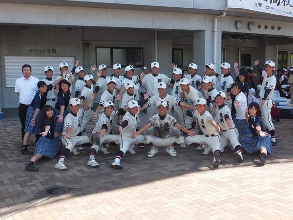 笑顔の篠山鳳鳴高校軟式野球部の選手が、球場入り口前で、両手を広げてポーズをとっている集合写真