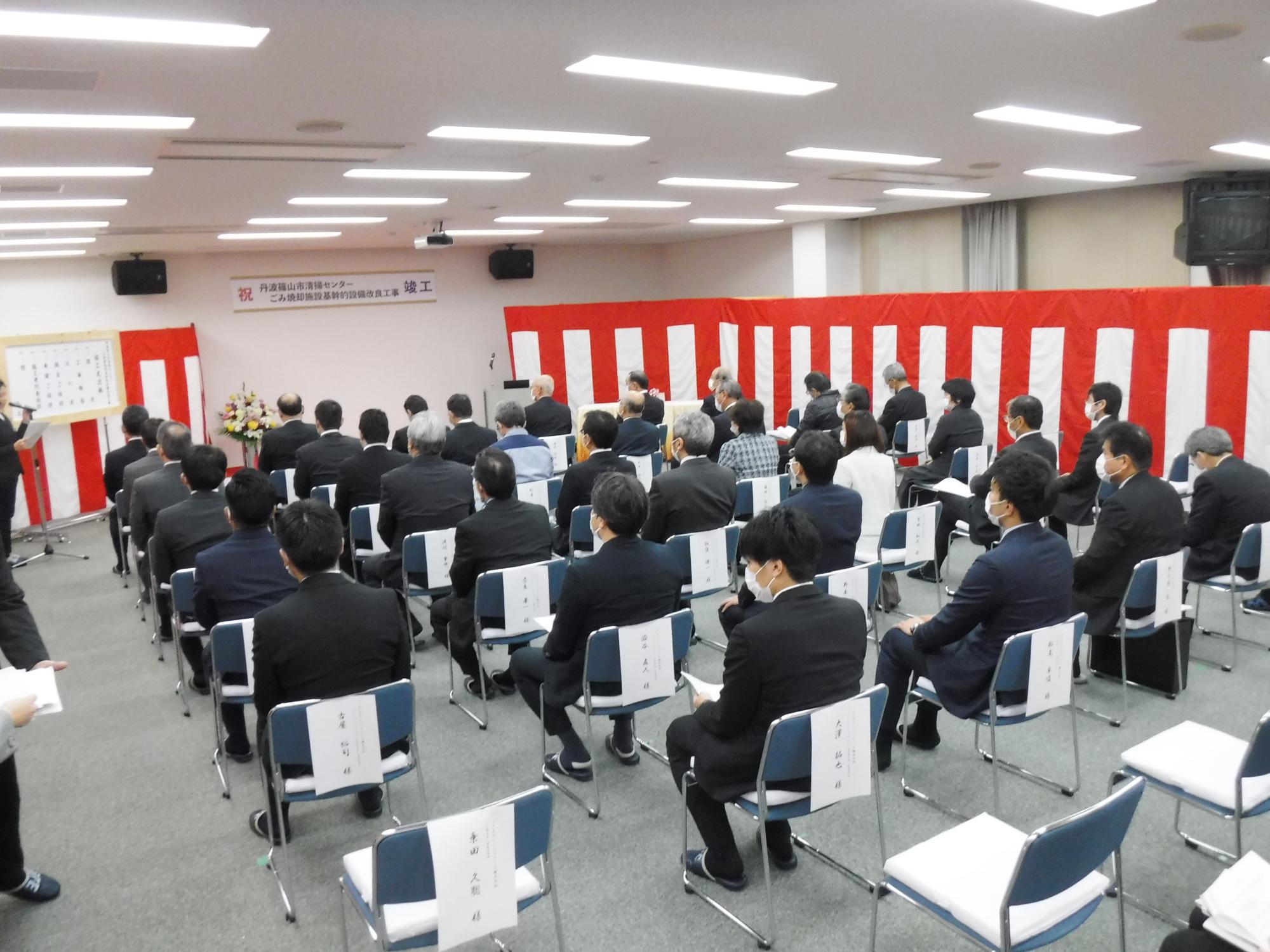 出席した人が並んで座っており、その会場を後ろから撮った写真