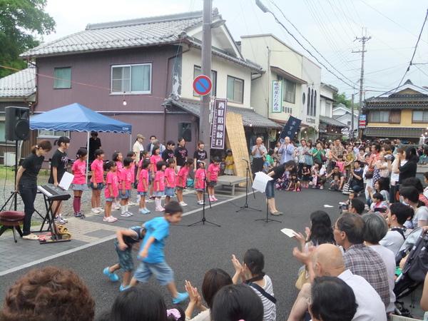 ピンクのティシャッを着た子供達が道路に集まっているお客さんにお辞儀している写真