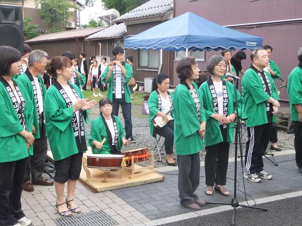 丹波篠山デカンショ祭りと書かれた緑の法被姿で太鼓や笛、三味線などを使って演奏している写真