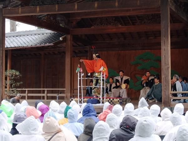 春日神社の能舞台で「篠山春日能」が行われている様子とレインコート姿で観覧しているの人たちの写真