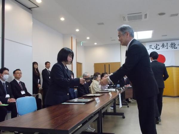 制服を着た女子学生がスーツの男性から表彰されている写真