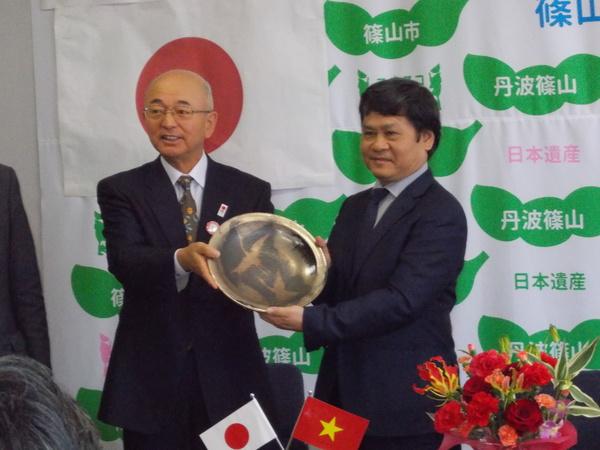 市長とスーツ姿の男性が二人で金色の丸いプレートを持っている写真