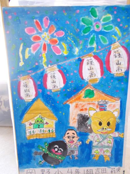 花火が上がり屋台が並ぶ祭り会場で楽しんでいる市長とゆるきゃらの絵が上手に描かれているあんどんの写真