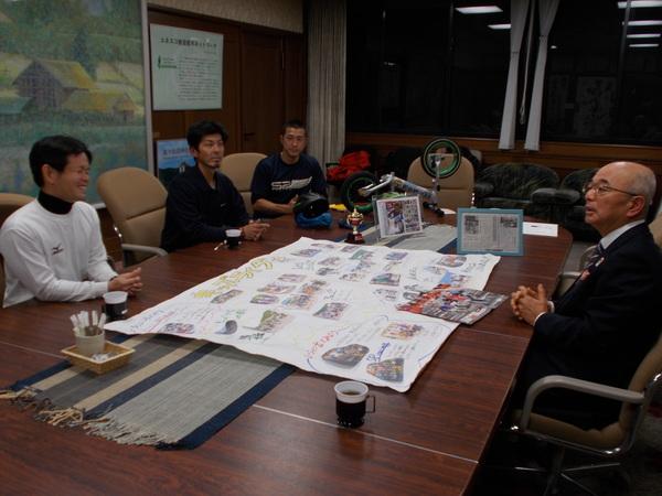 こんにちは市長室に、チーム「キッズライダー」が来て、机の上の写真や紹介などが書かれた模造紙を見ながら市長と話をしている写真