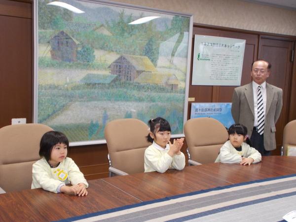 黄色いスモックを着た園児3名が、市長室の大きな椅子に座っている様子の写真