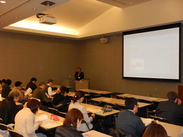 会議室のような場所でプロジェクターのスクリーンを見ながら研修を受けている医療従事者の人達の様子