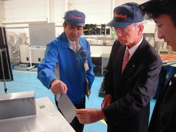 株式会社タカトリの社員から説明を受けている、タカトリのキャップをかぶった酒井市長と職員の写真