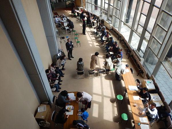 番号が置かれた机の横で、順番待ちをしている人々を上から写した写真