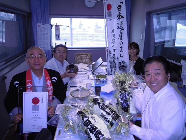 市長、三上 公也さん、池田 奈月さん、田辺 眞人さんが、それぞれ旗や、陶器、枝豆、透明なフレームに入った認定証を持っている写真