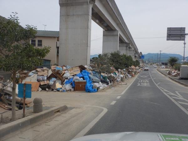 災害で出た廃棄物が道路際に積み上げられ、遠くまで続いている様子の写真