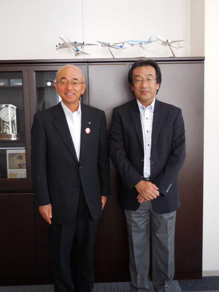 飛行機の模型が乗っている家具の前で、市長と酒井 淳さんとのツーショット写真