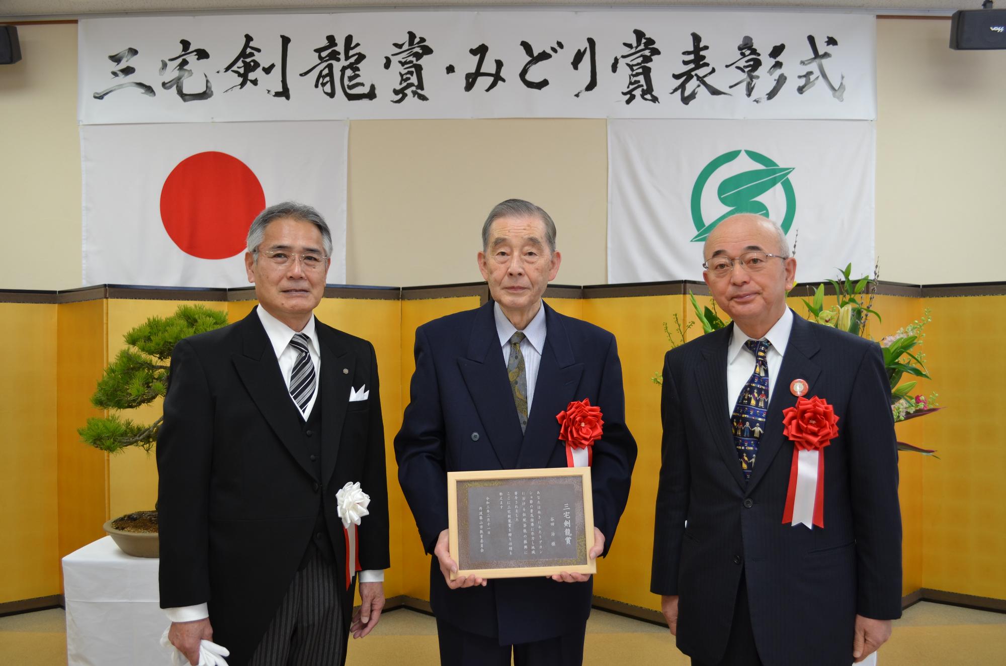 教育長と市長、表彰盾を手に持つ谷田さん。