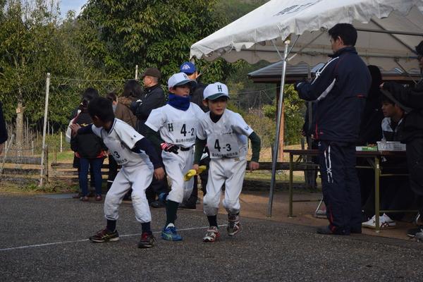 野球のユニフォームを着た男の子たちが一生懸命タスキをつないでいる写真