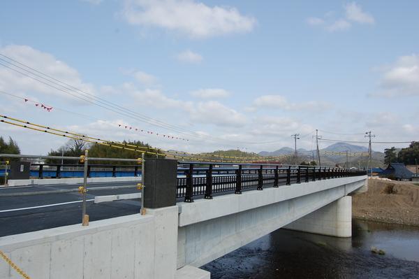 川の上に黒い柱で出来た橋がかかっている写真