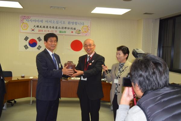 韓国郡守のホギドさんと一緒に壺を持っている市長が女性にインタビューされている様子をカメラマンが撮影している写真