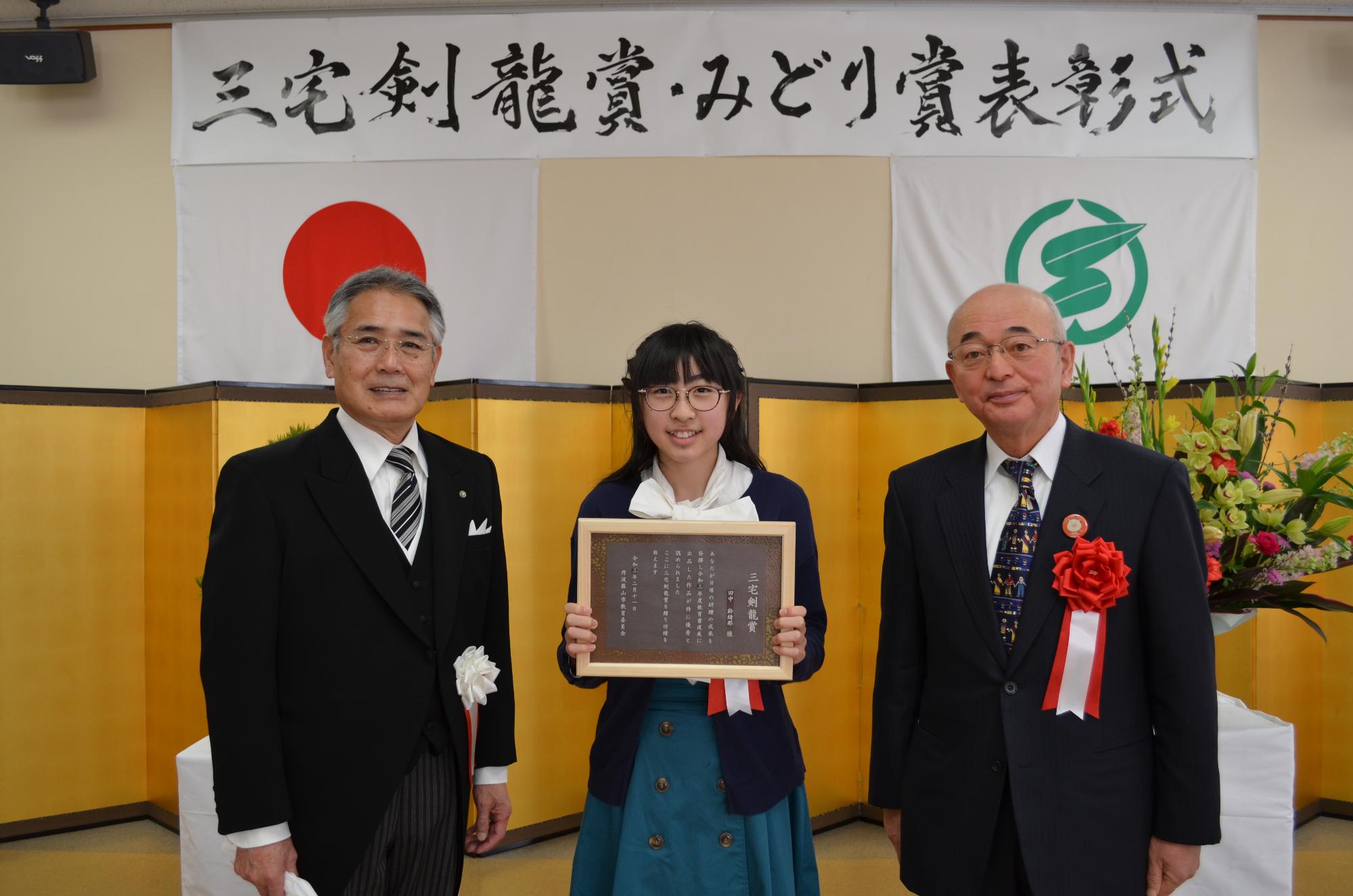 教育長と市長、表彰盾を手に持つ田中さん。