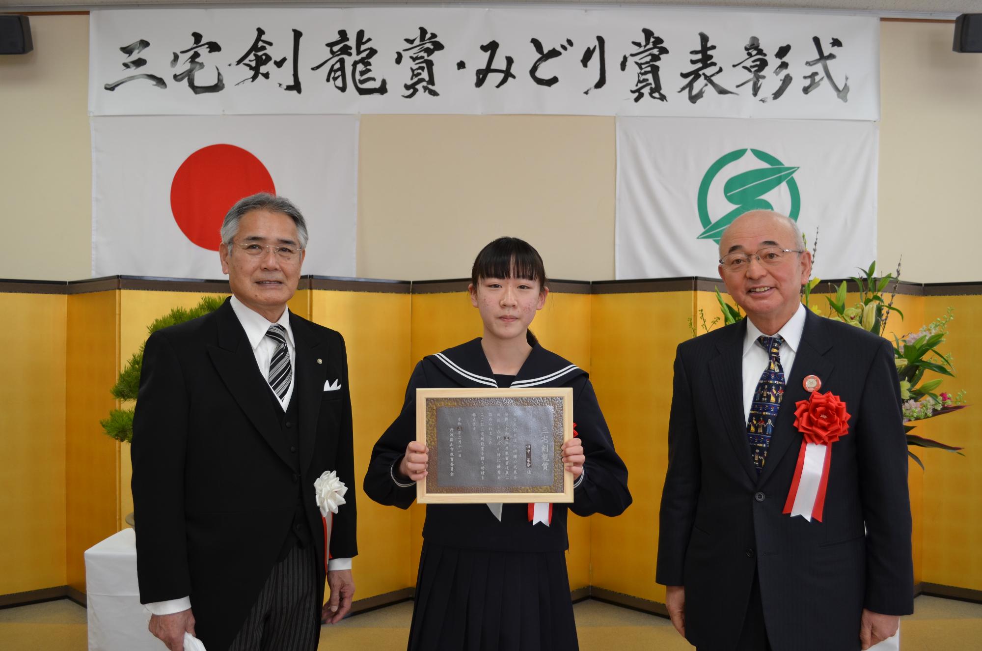 教育長と市長、表彰盾を手に持つ田中さん。