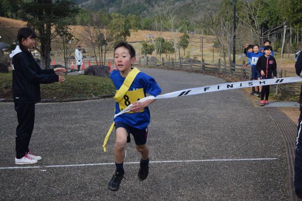 青いシャツの男の子がゴールテープを切っている写真