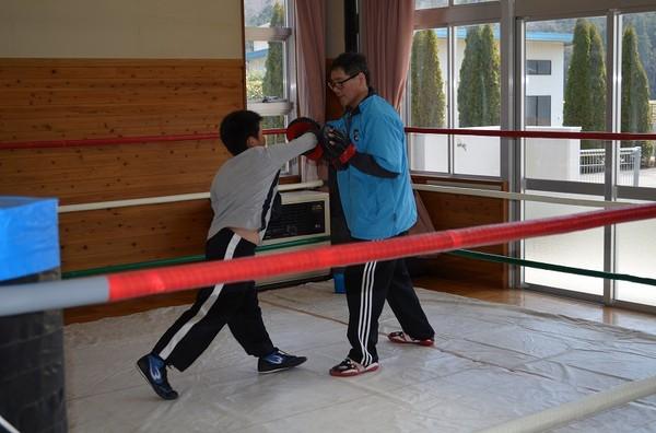 リングで子供の生徒がグローブを付けて指導者へ右パンチしている写真