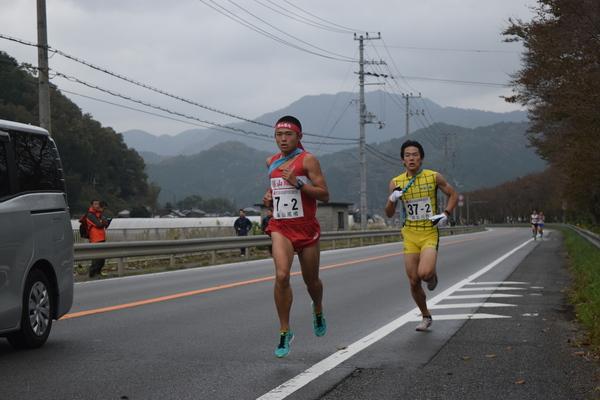 赤いユニフォームを着て走る高山 優明君と、その後ろから迫るを走りをする黄色いユニフォームを着た選手の写真