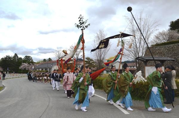 装束を着た人達を先頭に後ろから神輿を担ぐ人や子供達が歩いている写真