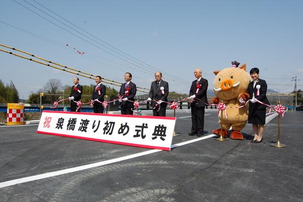 市長やまるいのの着ぐるみやスーツを着た男性達がテープカットをしている写真