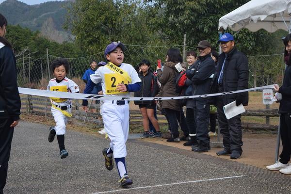 野球のユニフォームを着た男の子があと少しでゴールテープを切ろうとしている写真