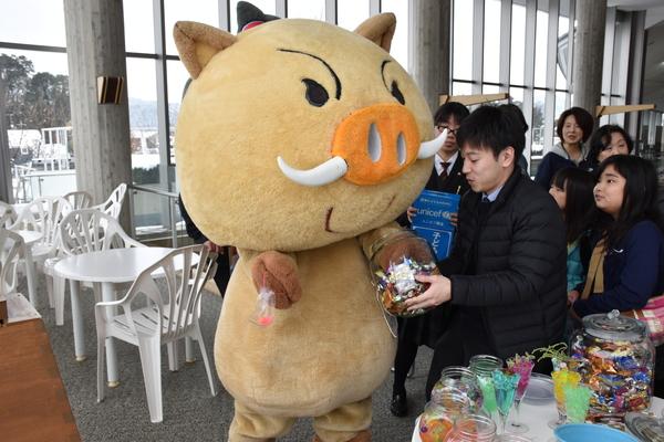 男性が持っているお菓子が入った透明な瓶にゆるキャラが手を入れている写真