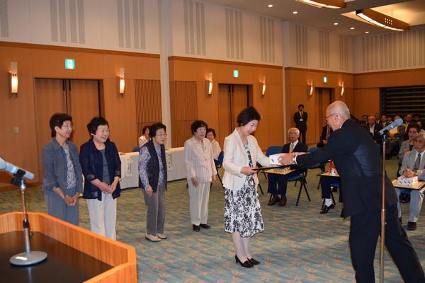 受賞者の女性が市長より表彰を授与しているところを他の受賞者が後ろに並び見ている写真