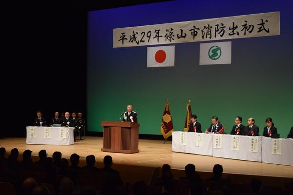 篠山市消防出初式で男性が舞台の上でお話をされて来賓の方はそのお話を聞いてる写真