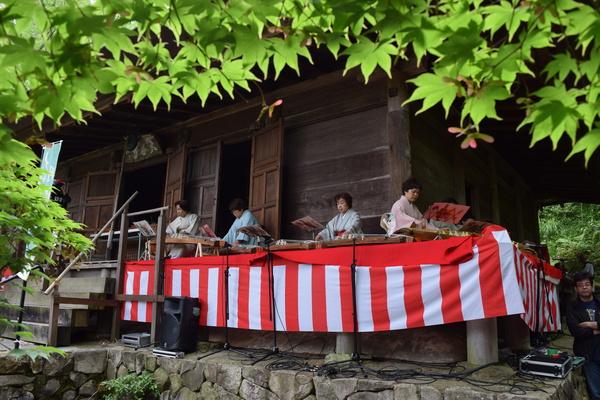 軒下に紅白幕が張られており、その上で4名の女性がお琴を弾いている写真