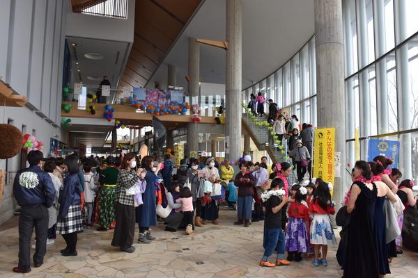 市民センターのフロアでフラダンスの出番を待っている団体と祭りの来場者の写真
