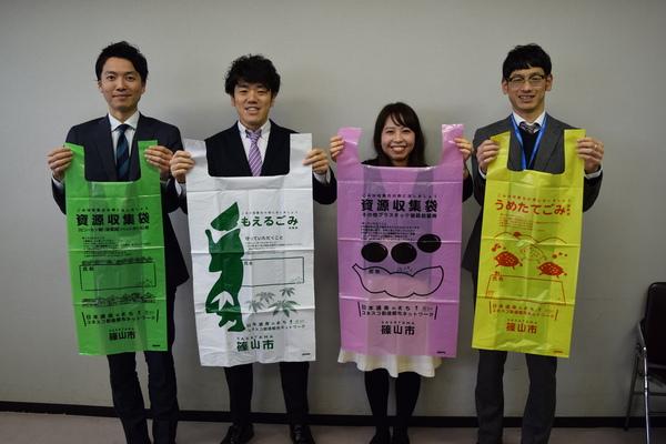 一新したごみ袋（緑、白、ピンク、黄色）を持った自治体の方々の写真