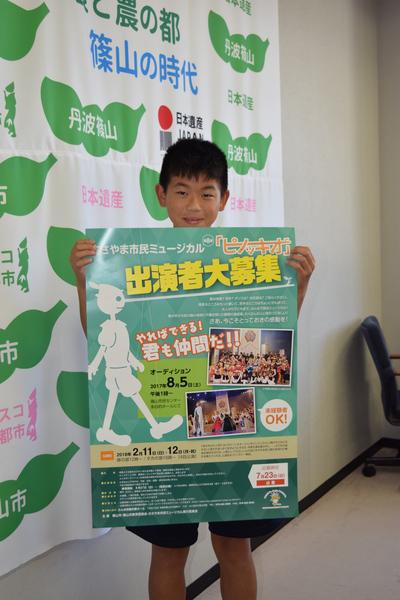 ささやま市民ミュージカルのポスターを両手で持ち笑顔で写っている小林 大輝くんの写真