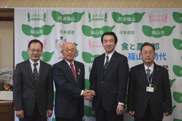 スーツ姿の男性3人と市長が並んでいて、市長とその右横の男性が握手をしている写真