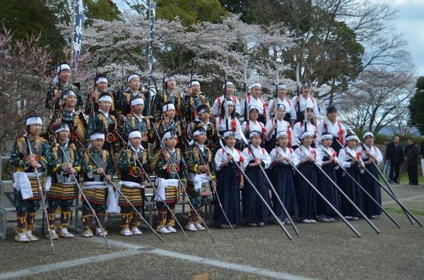 鎧を着た男の子たちと袴姿の女の子たちが大きな槍を持ってみんなで記念撮影写真