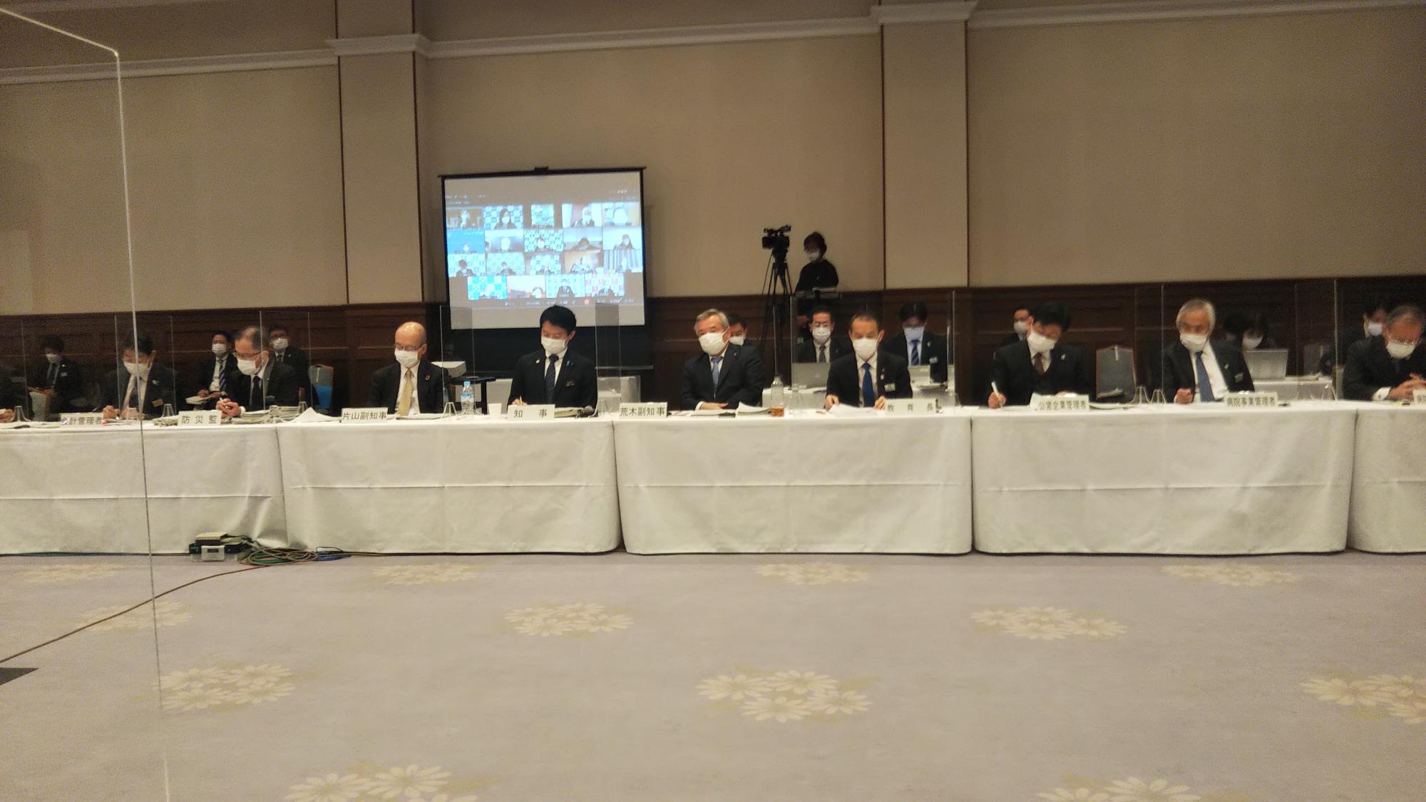 モニターの前に、県知事や幹部の職員が並んで座っている