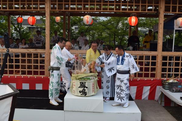 舞台の上で市長と浴衣を着た人たちが祝い樽の上板を叩いている写真