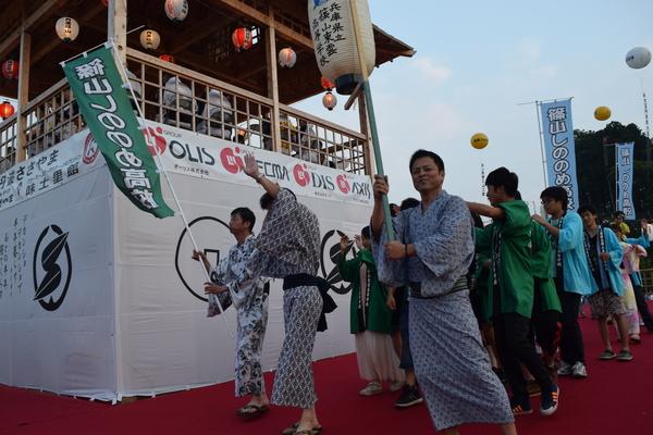 浴衣を着た男の人たちがのぼり旗や提灯を持って歩いている写真