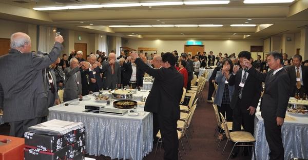 テーブルに料理が並んでいる会場でグラスを片手に乾杯が行われている写真