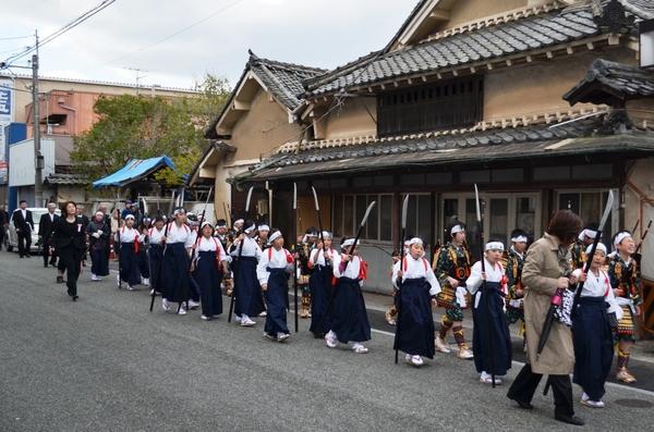 大人に連れられ鎧と袴姿の子供達が町を歩いている写真