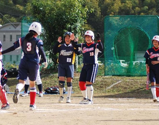 ソフトボールの試合で、走者がホームインし、メンバーとハイタッチしようとしている