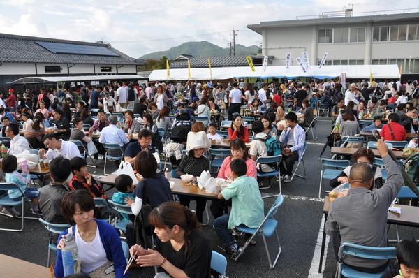 沢山の人が、並べられた席や、テントの前に集まる写真