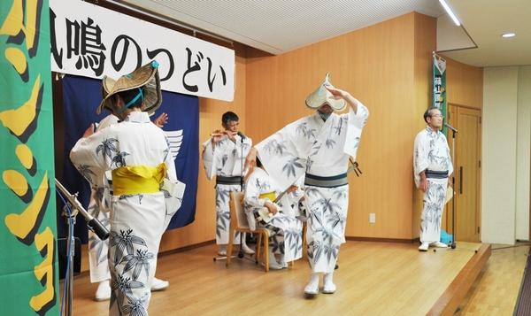 編み笠に浴衣姿の男性らが横笛と三味線に合わせて舞台で踊っている写真