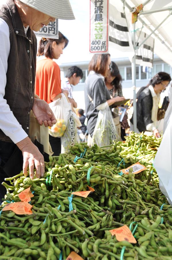 購入した枝豆が入った袋を手にするお客さんと、たくさん積まれた枝豆を手にする女性の写真