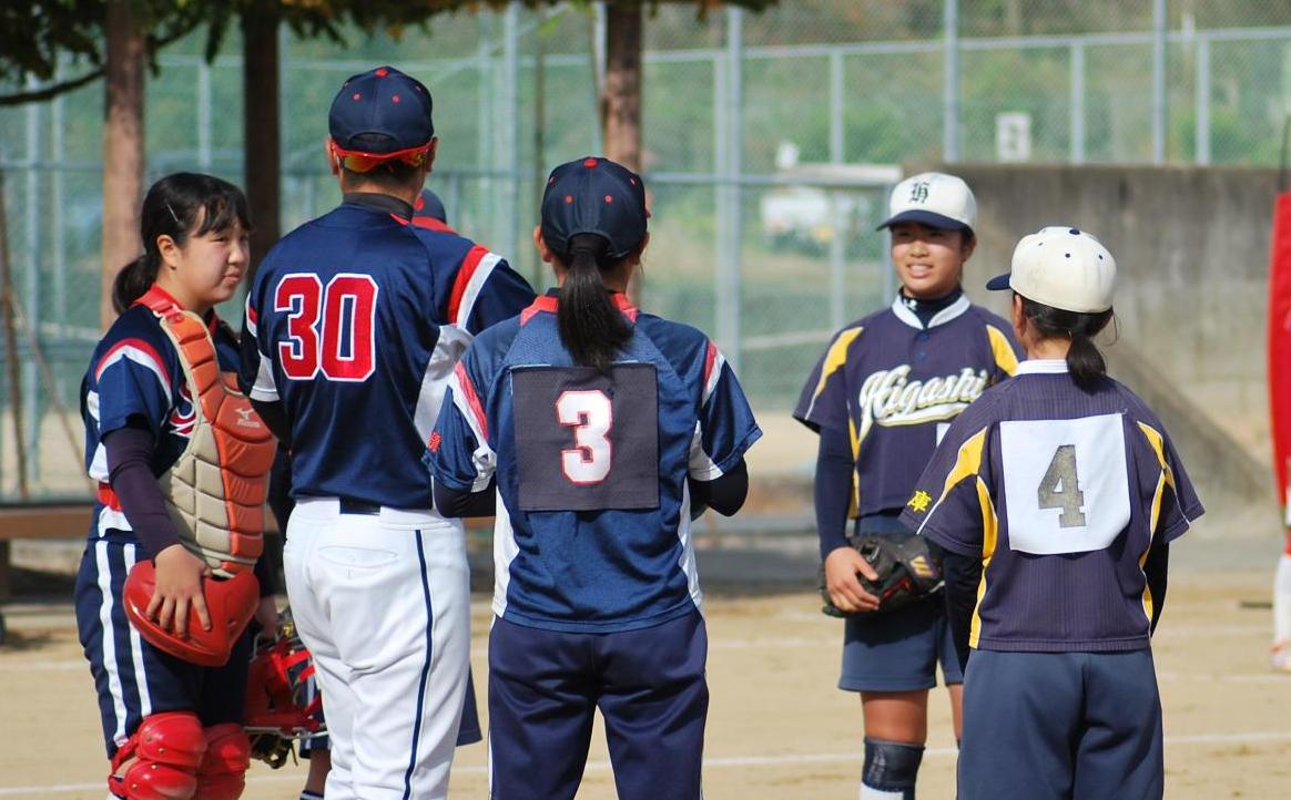 ソフトボールの試合で、監督が輪になった部員に指示を出している