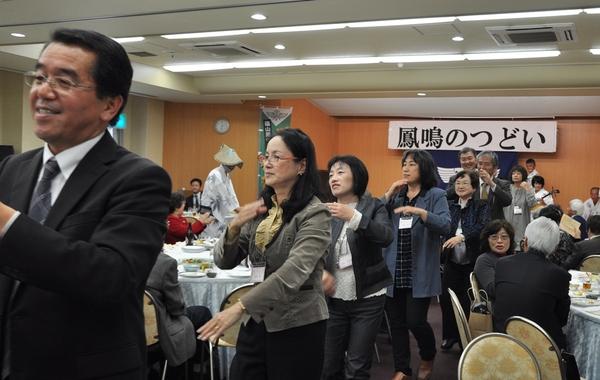 宴会会場で三味線に合わせて踊る人々の写真
